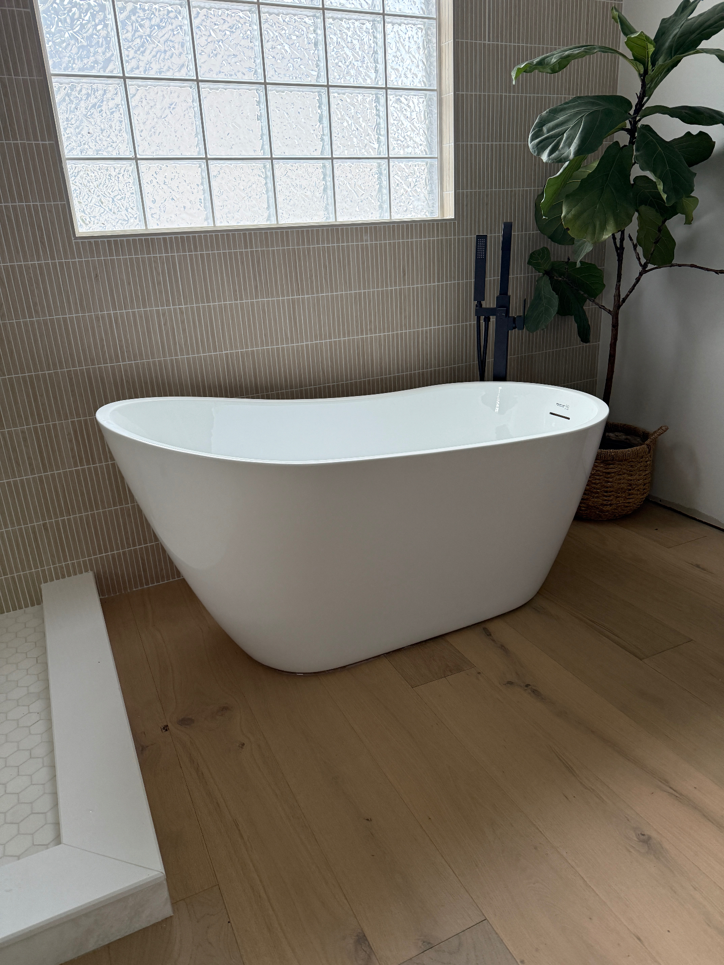 Freestanding tub with matte black filler beside a glass block window