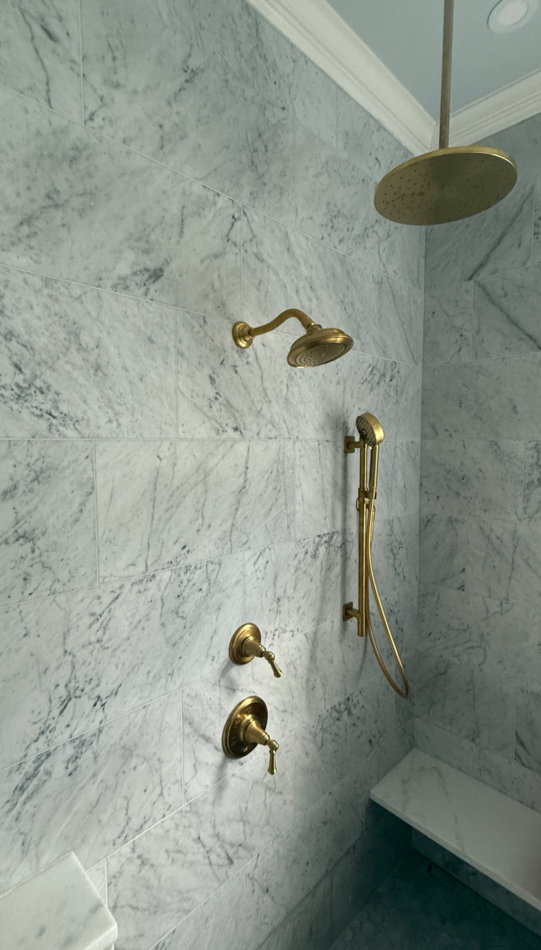Brass shower system with rainfall head and hand shower in a tiled marble shower
