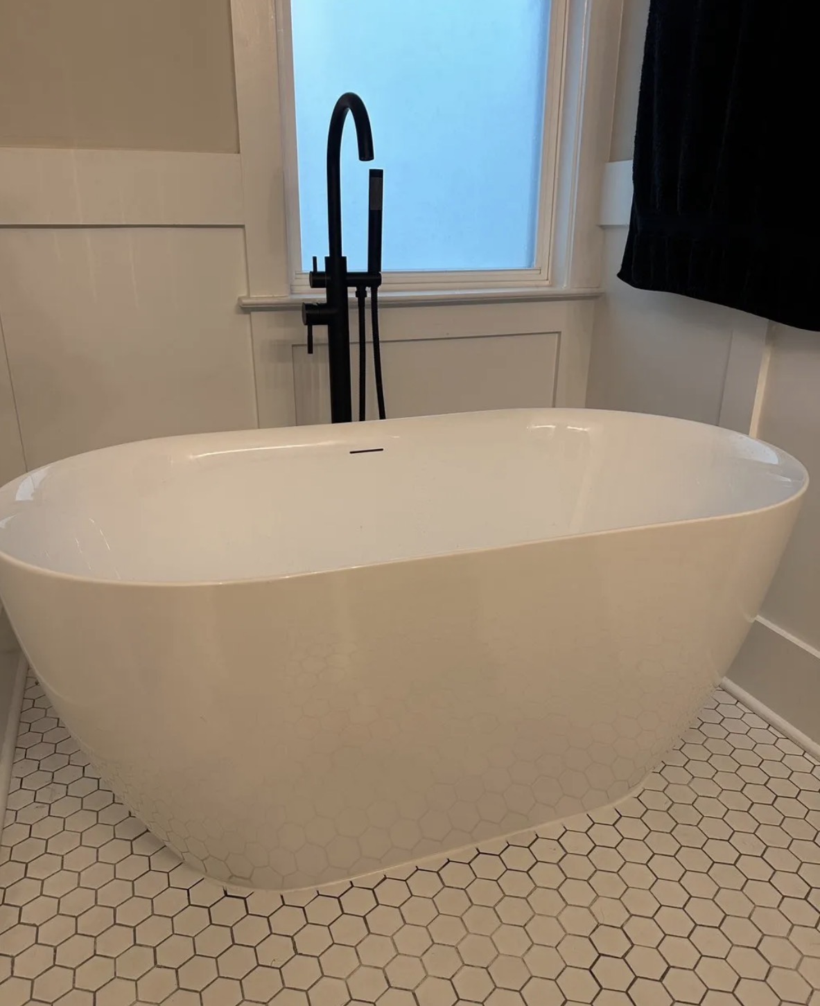 White freestanding tub with matte black floor-mounted filler on hex tile floor
