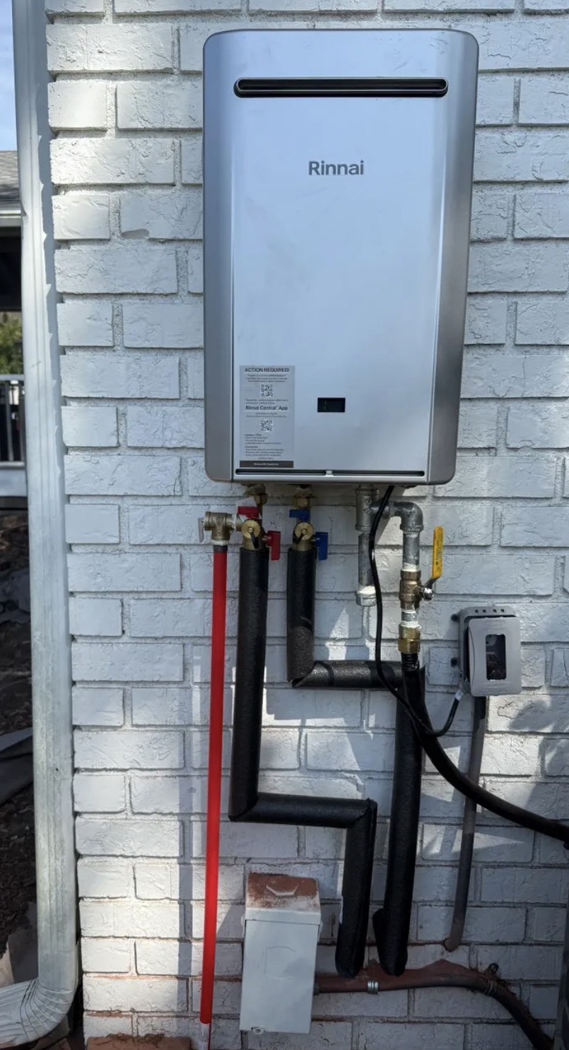 Rinnai tankless water heater mounted on a brick exterior wall with insulated supply lines