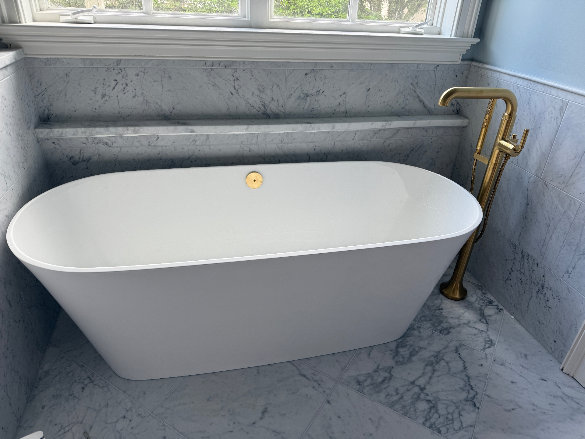 Freestanding tub with brass floor-mounted filler in a finished marble bathroom