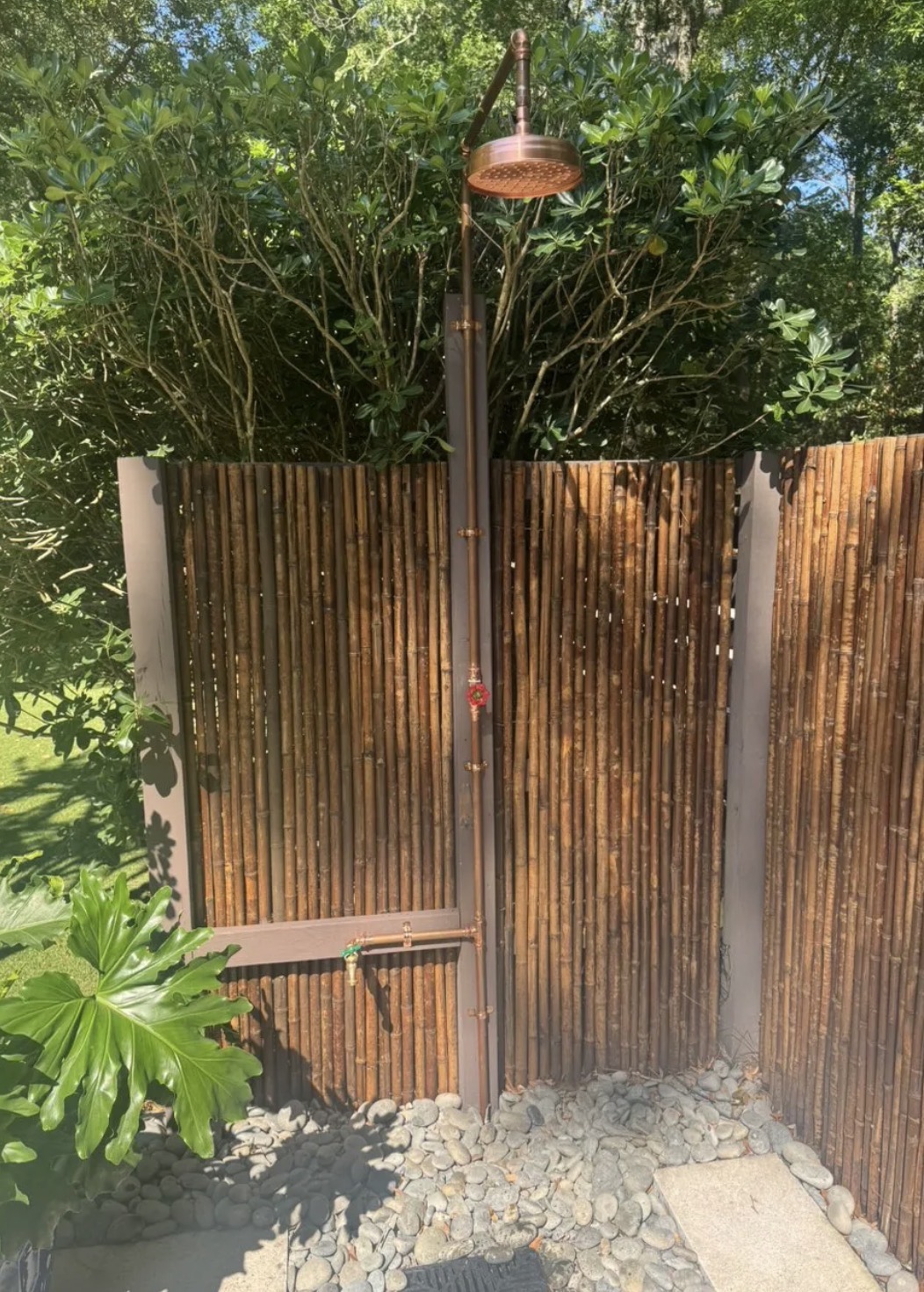Copper outdoor shower installed against a privacy screen in a landscaped yard
