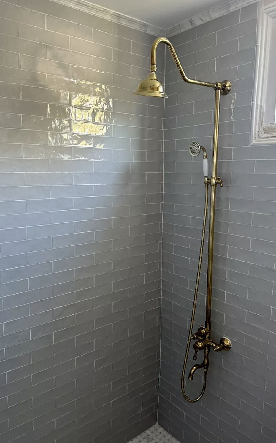 Antique brass exposed shower system with rainfall head and hand shower on gray subway tile